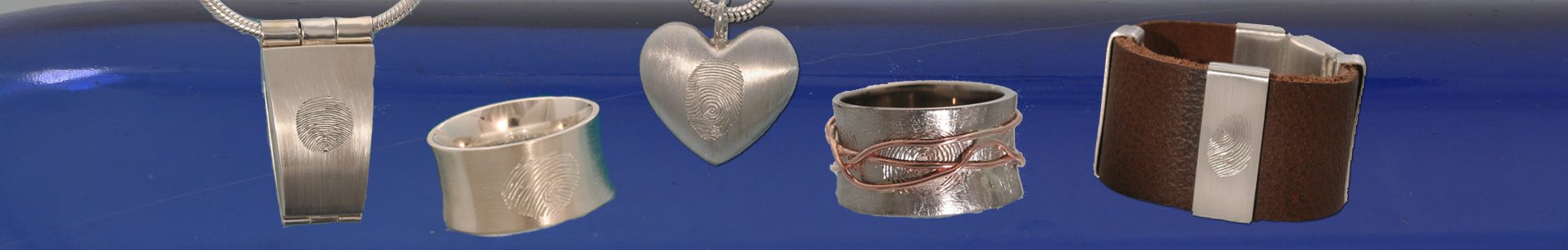 Last Touch.Een medaillon met een vingerafdruk, een ring met een vingerafdruk, een wikkelring met onder de roodgouden draad een vingerafdruk en een lederen armband met een zilveren lus, met hierop een vingerafdruk