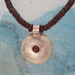 Een zilveren hanger met granaat, hangend aan een snoer granaatkralen, de hanger heeft een doorsnede van 23 mm. Prijs: €260,- Granaatcollier