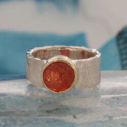 Een zilveren ring met een zonnesteen gezet in een geelgouden kastje