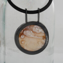 Een gezwarte zilveren hanger met parelmoer met vergroeide parels. hangend aan een lederen snoer.