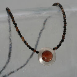 Een fijn collier van bruine en zwarte onyx kraaltjes en een zilveren hanger met zonnesteen