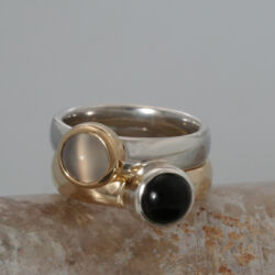 Een zilveren ring met in een geelgouden zetkastje een maansteen en een geelgouden ring met in een zilveren zetkastje een onyx