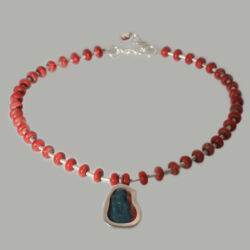 Aya
Een collier van bamboo-koraal kralen met zilveren tussenstukjes en een zilveren hanger met een glazen scherf.
De scherf is uit de plomeïsche periode, Egypte 0- 300 voor het begin van de jaartelling. De hanger is 24 mm hoog. Plomeïsche periode