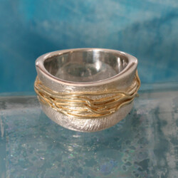 Als levenspaden omwikkelen de geelgouden draden de golvende zilveren ring van 12 mm. Prijs: €685,- Goud en zilveren wikkelring