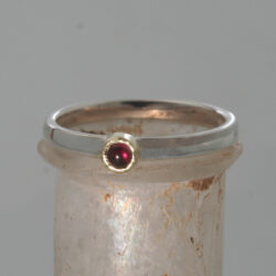 Een zilveren ring met een cabouchon geslepen robijn een een geelgouden zetkastje. De ring kan als aanschuifring gecombineerd worden. Prijs: €370,-