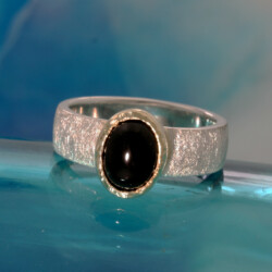 Een ijsmatte zilveren ring met een ovale cabouchon onix gezet in een geelgouden zetkast