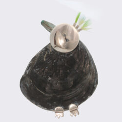 De strandschuiver. Een typische wadvogel. Echt goed vliegen kan hij niet, maar hij schuifelt eindeloos over stranden en droogvallende platen. Zijn kuifje is wat slordig en groen/turkoois. Gewoonlijk is de strandschuiver zwijgzaam, toch kan hij in een goede bui tevreden hummen. Zilveren broche met een fossiele platte oesterschelp, kyaniet en parkietenveertjes. Hoogte 7 cm. Prijs: €390,-