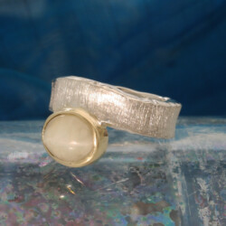 Een zilveren ring met een ovale kwartskattenoog gezet in een geelgouden zetkast.