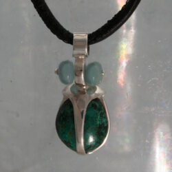 De chrysocolla-kever komt voor in de Oeral, Rusland en zuid-Amerika. Het is een zachtaardig diertje, wat graag scharrelt in laag grasland. De hanger is gemaakt van zilver, chrysocolla en amazoniet. De hanger is 30 mm hoog
Prijs exclusief collier € 165,-