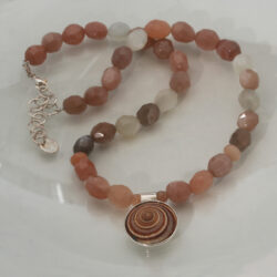 Een collier van zonnesteenkralen met een zilveren hanger met een zonneslak. Prijs € 250,-